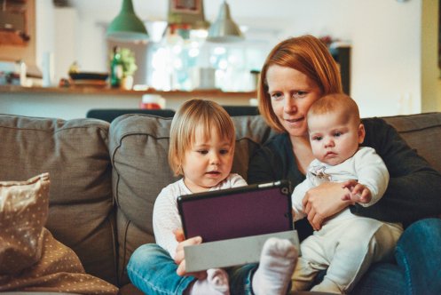en kvinna sitter i en soffa med två små barn och tittar i en iPad.