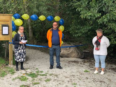 Tre personer på rad på en stig med ett blått band som ska klippas. Träd och gula och blå ballonger i bakgrunden.