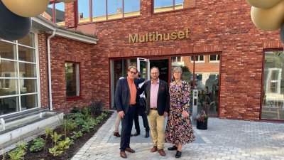 Två män och en kvinna framför Multihuset i rött tegel. Plan.tering till vänster
