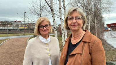 Två kvinnor står utomhus, tittar mot kameran och ler.