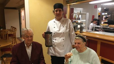 Stig och Elsa sitter vid bordet. anna-Karin står mellan dem med kaffekannan.