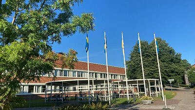 Ukarinas flagga i mitten av fyra svenska flaggor´framför stadshuset. Blå fimmel och gröna träd i förgrunden och bakgrunden.