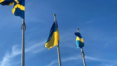 Tre flaggstänger mot blå himmel. Sveriges flagga på två av dem, Ukrainas flagga i mitten.