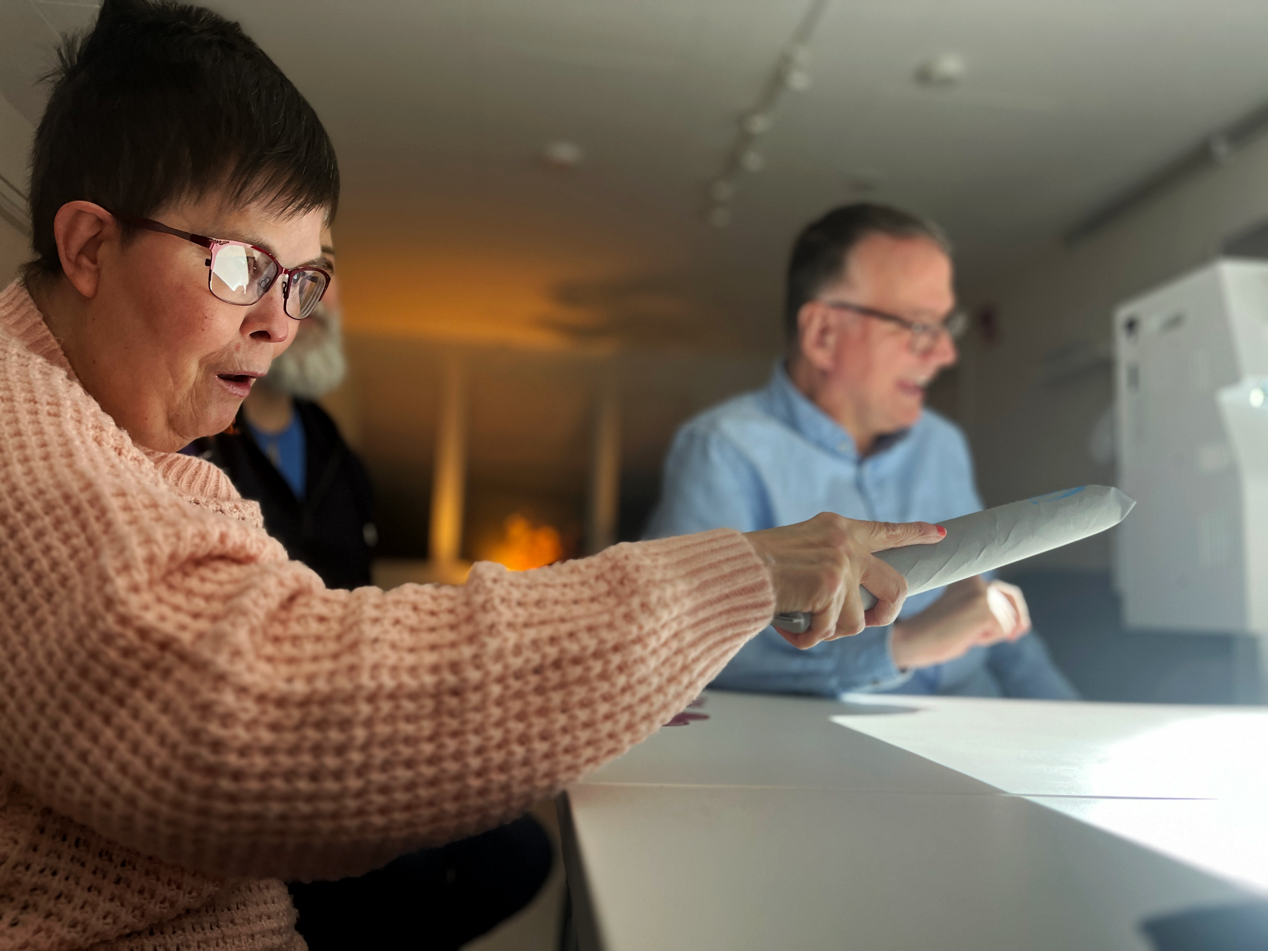 En kvinna sitter vid borde och håller i ett föremål som hjälper henne att interagera med bilderna som projiceras på bordet.