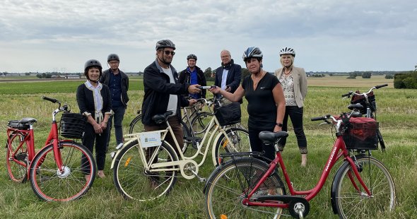 Sex personer står vid sina cyklar med Karaby backar i bakgrunden