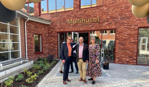 Två män och en kvinna framför Multihuset i rött tegel. Plan.tering till vänster