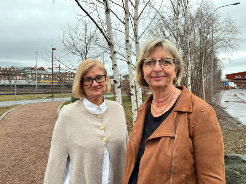 Två kvinnor står utomhus, tittar mot kameran och ler.