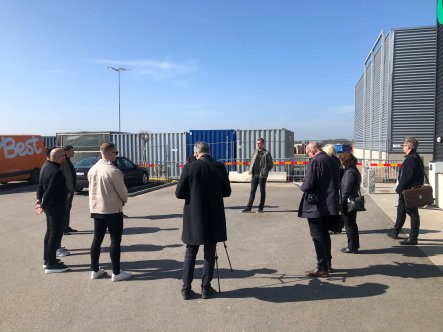 Personer som står i en ring runt David Mårtensson. Byggnad och containrar i bakgrunden.